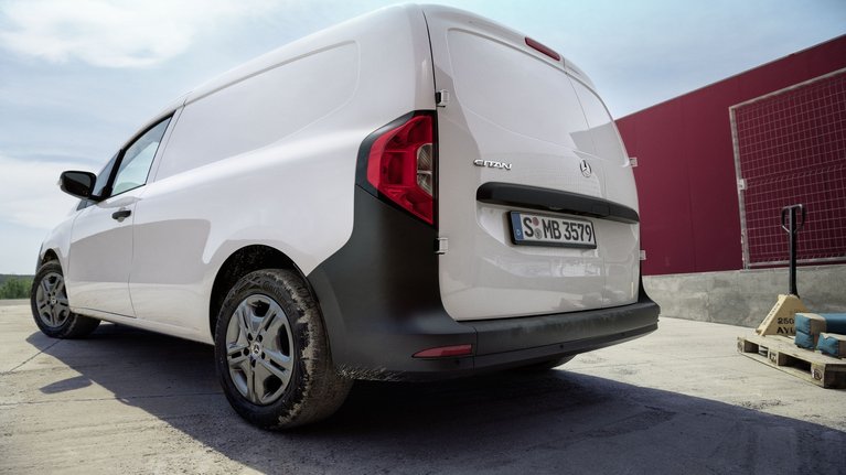 Mercedes-Benz Citan Kastenwagen in Weiß, Heckansicht auf einer Baustelle mit rotem Gebäude im Hintergrund.