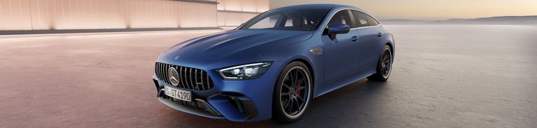 Mercedes-AMG GT 4-Türer Coupé in mattem Blau, geparkt vor einer beleuchteten Architektur bei Sonnenuntergang, betont die dynamische Silhouette des Sportwagens.