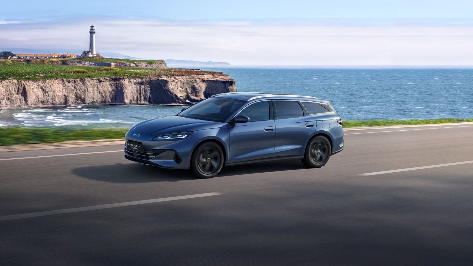 Ein blauer BYD Seal 6 DM-i Touring fährt auf einer Küstenstraße entlang des Meeres, mit Klippen und einem Leuchtturm im Hintergrund.